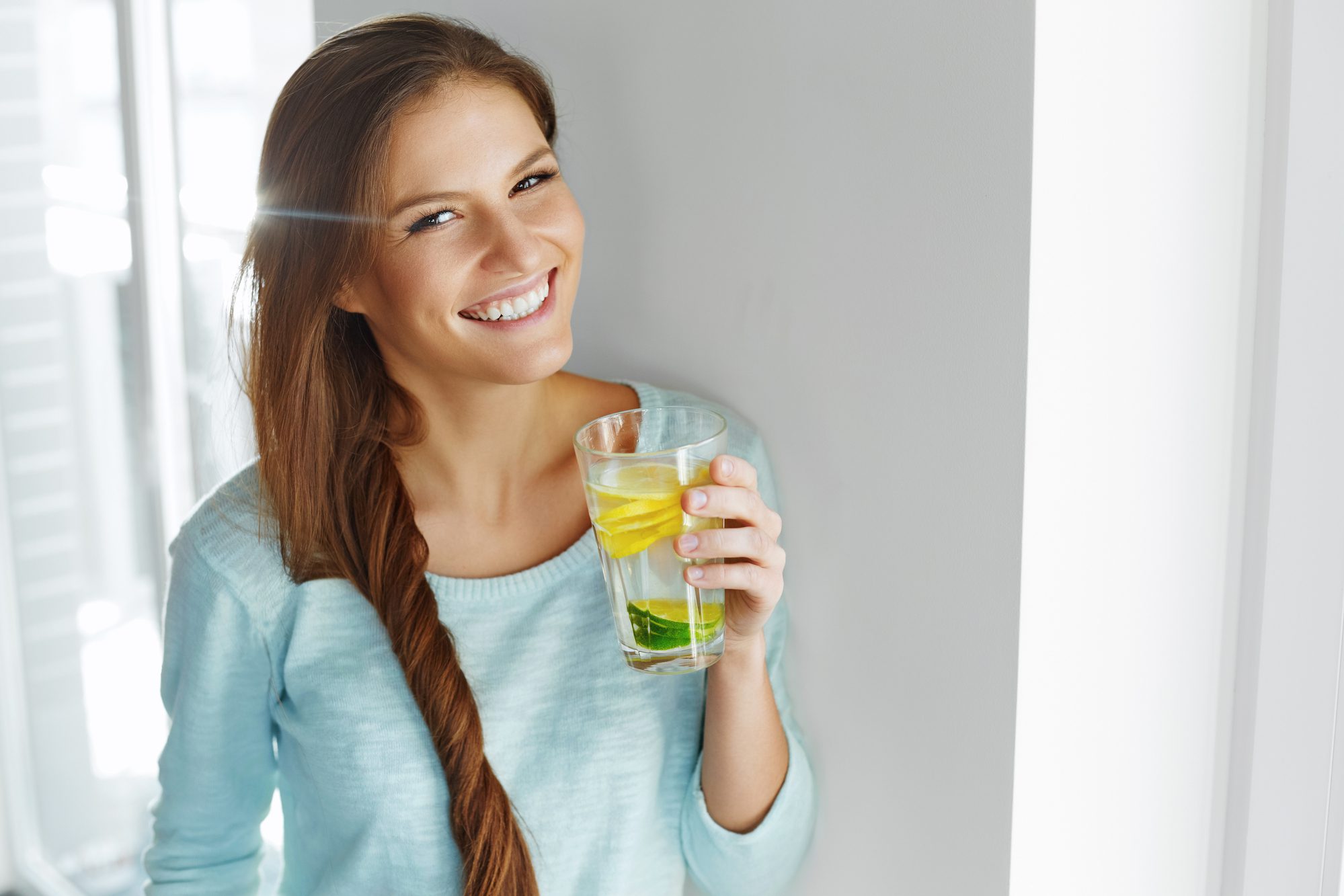 Jeune femme souriante boit un verre d'eau détox au citron